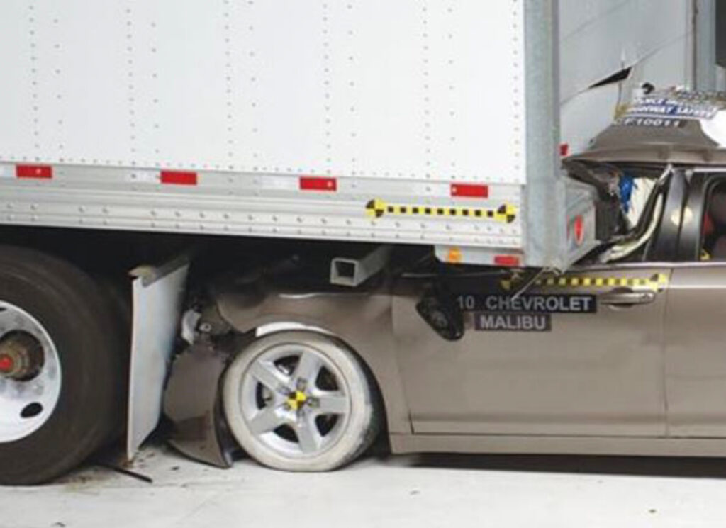 Tan Chevrolet Malibu crashed into and under the back-end of a semi-trailer.